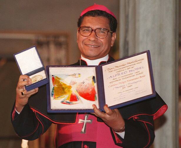 bishop belo of dili, east timor, holds his nobel peace prize in a 1996 photo, he wears his bishops' clothes with a purple hat and belt