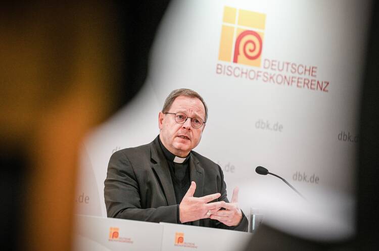 bishop georg bätzing sits in front of a microphone at the conference of the german bishops, he wears his priest clothing and is gesturing with his hands