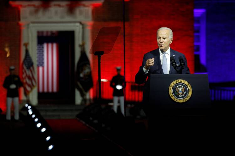 joe biden stands while giving his speech on maga republicans, the background behind him is red with an american flag