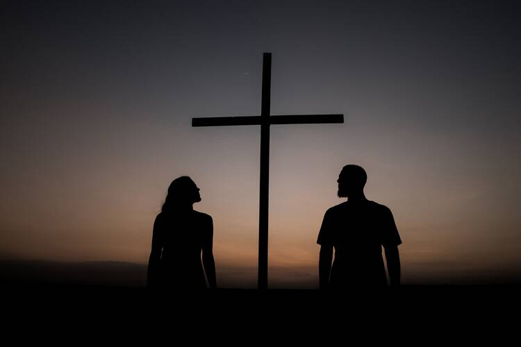 Two people look upon a cross at dusk.