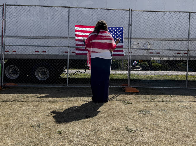 A woman prays as she faces a U.S. flag on a perimeter fence