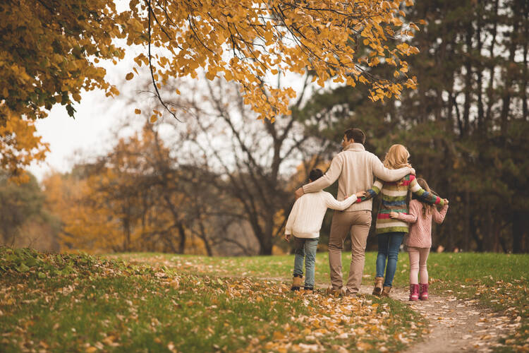 family of four walking away from camera in an autumn park, the trees have yellow leaves and the grass is green with yellow leaves on it