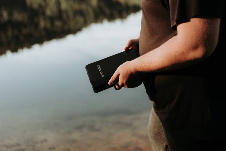 person holding a bible in front of a lake
