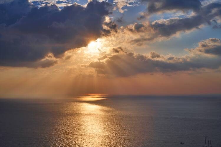 Sunlight peeking through clouds over the ocean.