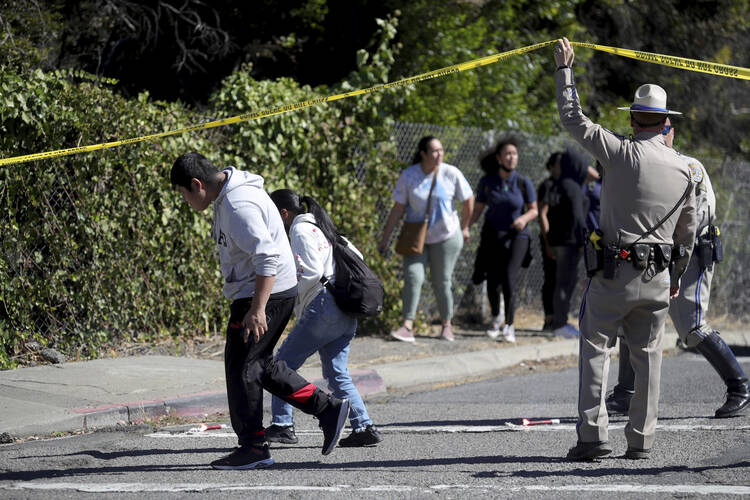 A California Highway Patrol officer lifts police tape to let parents and students leave a cordoned-off area following a shooting at a school campus in Oakland, Calif., on Sept. 28, 2022. (Ray Chavez/Bay Area News Group via AP)