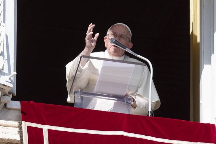 Pope Francis dressed in white garments holds a hand up while speaking to a crowd