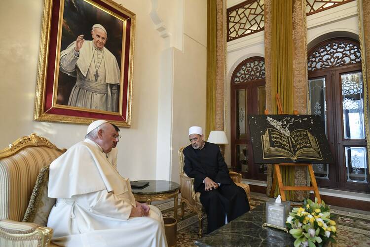 Pope Francis dressed in white garments sits speaking to Sheikh Ahmad el-Tayeb dressed in black with a white hat