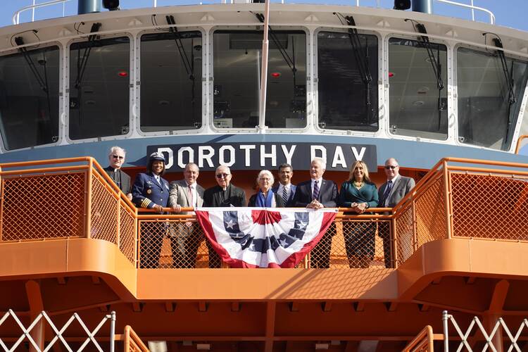 martha hennessy and other dignitaries stand on the hull of the dorothy day ferry boat in new york city with a flag in front of them