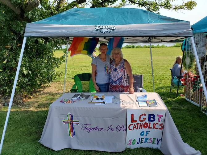 two people standing under an awning with an lgbt catholics of new jersey sign in front of them