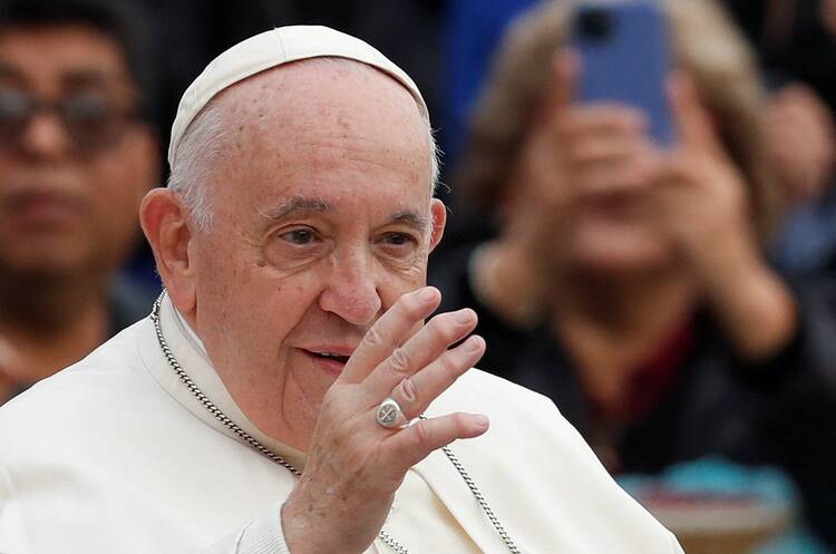 close up of pope francis face with hand in front raised in blessing, he is among people but they are blurred in the background