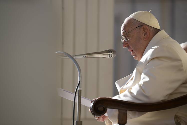 The pope, dressed in white garments, speaks into a microphone while seated