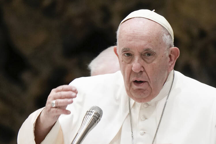 Pope Francis, dressed in white with a chain around his neck, speaks into a microphone