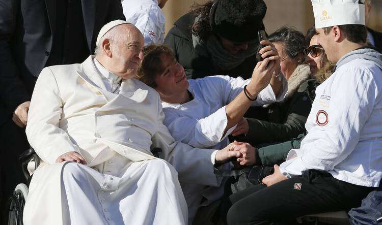 pope francis poses with a chef who is taking a selfie with him, he sits in his wheelchair