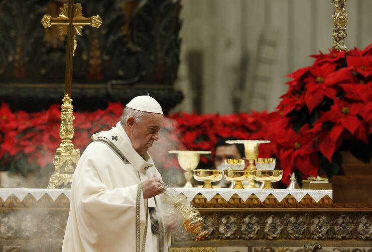 pope francis celebrates mass holding incense and thurible, red poinsettas are behind him
