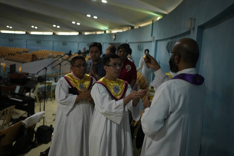 A line of altar servers receive Communion from a priest, all in white robes