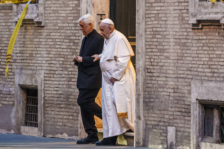 A priest dressed in black priest's garments assists the pope, wearing white papal robes
