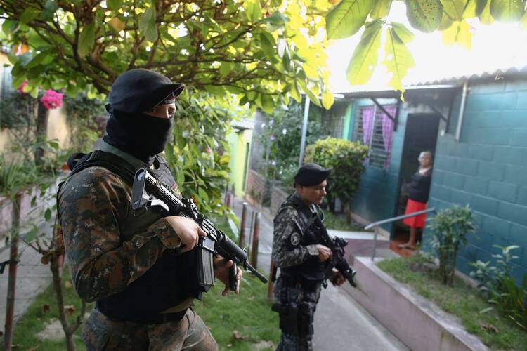 An elderly woman stands in her doorway as armed Salvadoran troops patrol a residential area in Soyapango on Dec. 5. A massive crackdown on gangs in El Salvador has led to ongoing human rights abuses, says a new report. (CNS photo/Jose Cabezas, Reuters)
