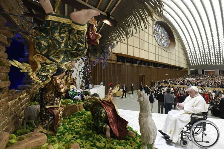 pope francis sits in his wheelchair in front of the nativity scene which is on the left of the photo in the vatican audience hall