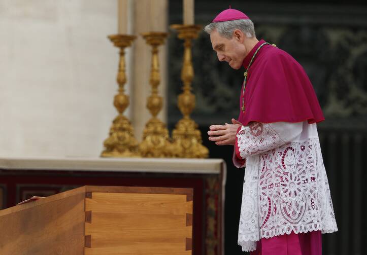 archbishop georg gaenswein stands next to the coffin of pope benedict while wearing full bishop garb of purple and white