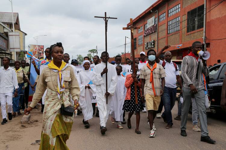 people stand in a crowd behind a cross, they are from democratic republic of the congo and wearing white clothing