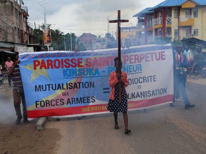 A woman carries a cross in front of a large banner
