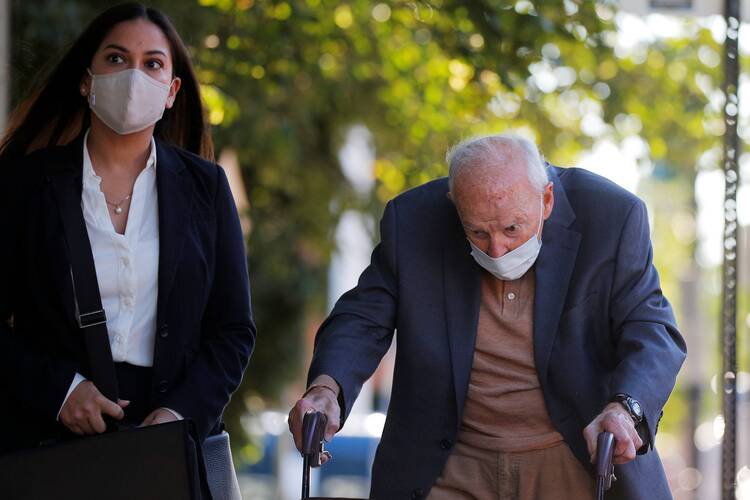 theodore mccarrick walks, hunched over, wearing a mask next to a young woman also wearing a mask. they are outside