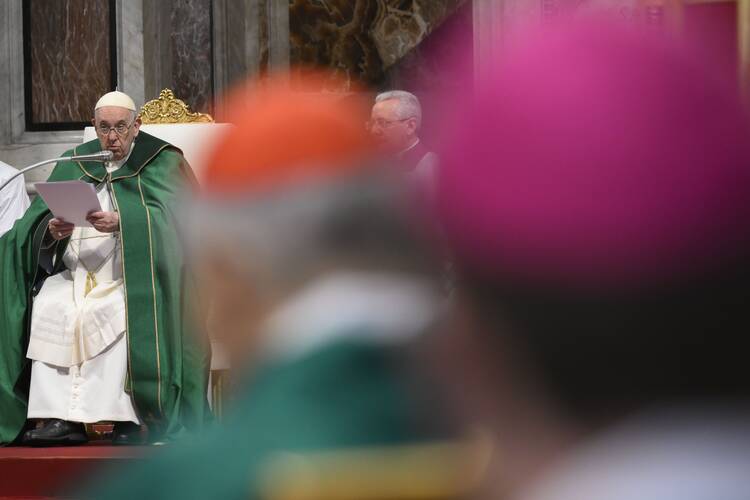 pope francis at left, with out of focus cardinals and bishops sitting in front of the camera