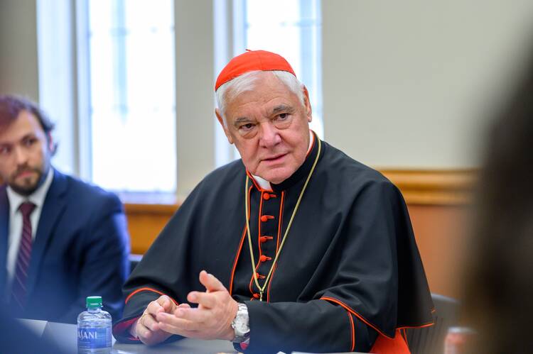 gerhard mueller wears his cardinal clothing with red cap and addresses students with a bright window behind him