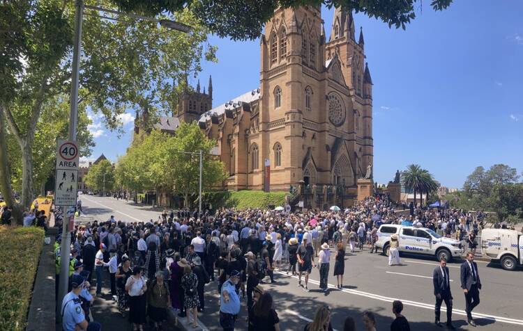 A crowd gathers to enter a beige church building