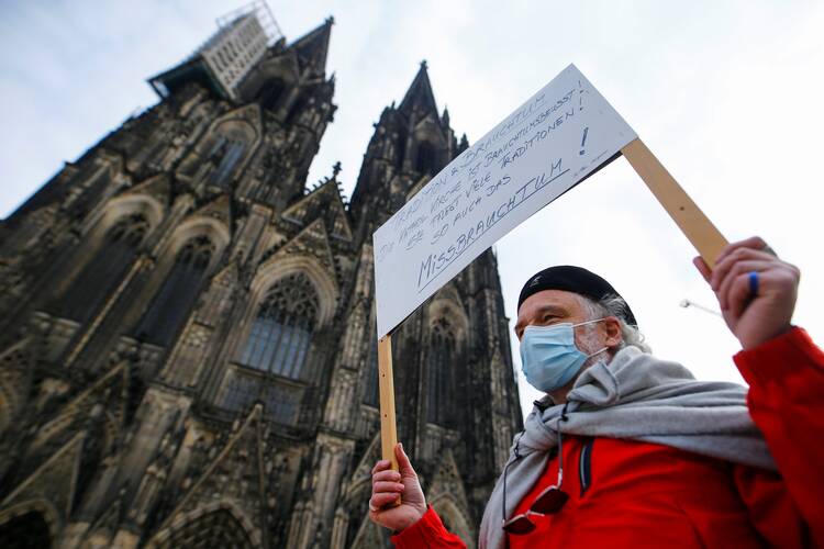 A demonstrator holds a placard reading “Tradition & Customs Catholic Church cares for tradition! Maintain many traditions! Such as abuse!” during a protest in front of the Cologne Cathedral in Germany.