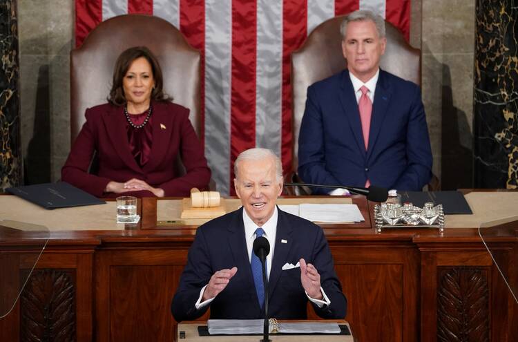 joe biden sits at front with kamala harris and kevin mccarthy sitting behind him, biden is talking with hands raised 