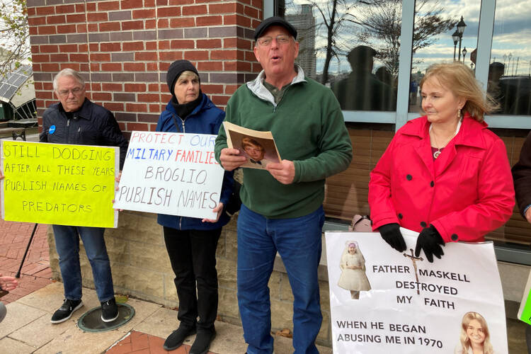people stand outside holding signs about priest accountability