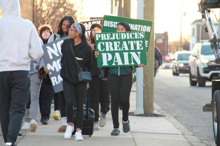 students protesting outside st hubert catholic school for girls, one holds a sign that reads "prejudices create pain"