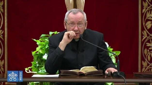 A man in black priest's garb speaks into a microphone