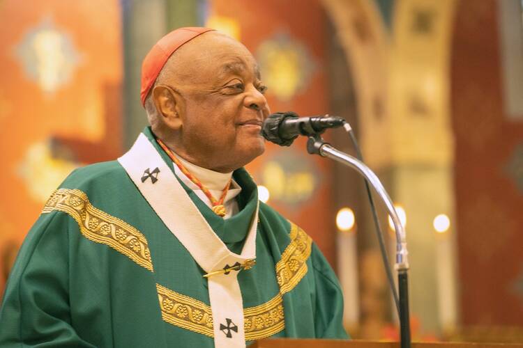 cardinal wilton gregory speaks at a microphone wearing green vestments and a red cap of an archbishop