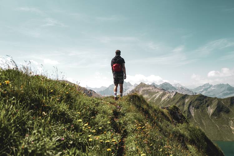 man hiking in grass among treetops and mountains