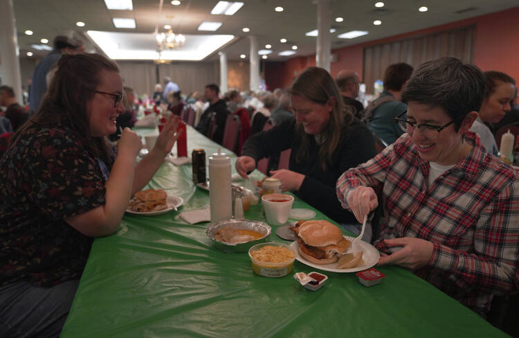 three people sit at a green-table-clothed table with fish sandwiches in front of them, smiling and talking