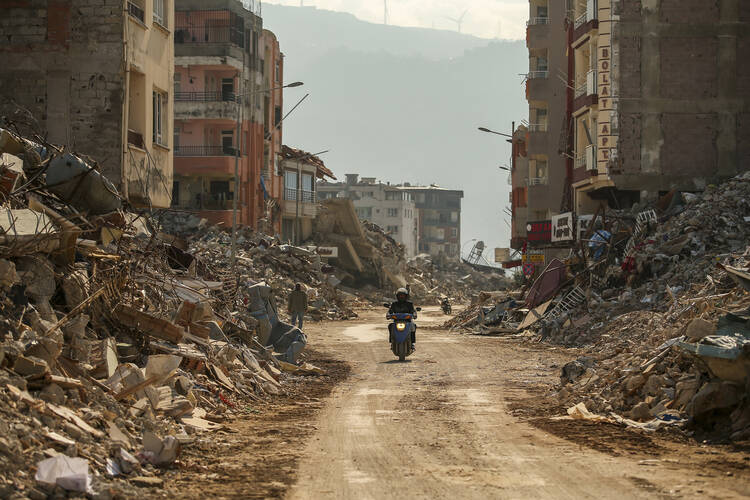 A man rides a motorcycle past debris from destroyed buildings in Samandag, southern Turkey, on Feb. 22, 2023. (AP Photo/Emrah Gurel)