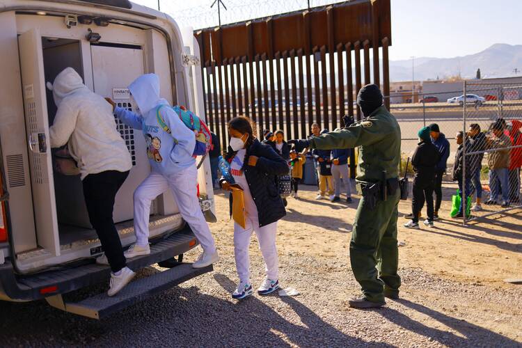 people going into a vehicle next to the border wall with mexico