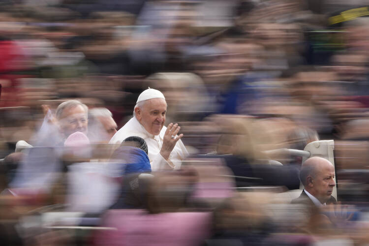pope francis is waving and in focus and everyone else around him is blurry in a photo with slow shutter speed at a general audience