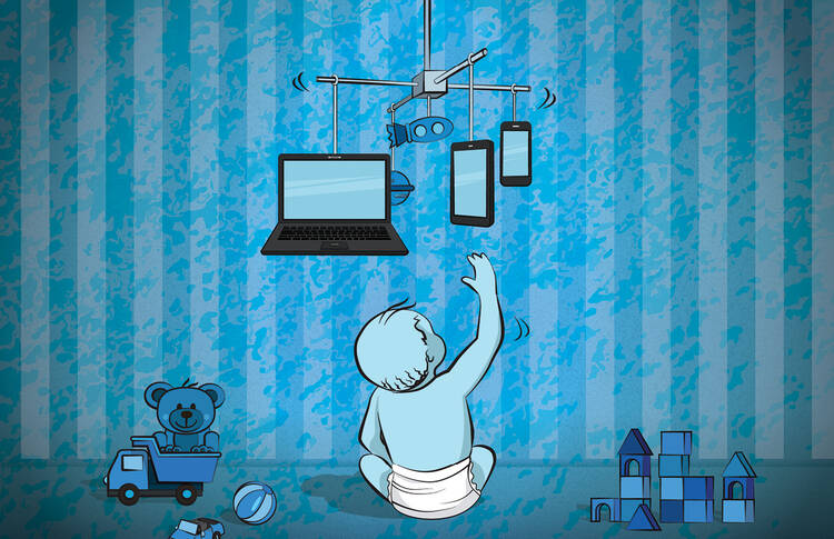 a child reaches up to a cot mobile with computers and phones hanging from it
