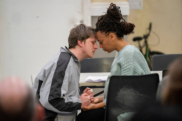 A man and woman sit close together and share an intimate moment in a play rehearsal .