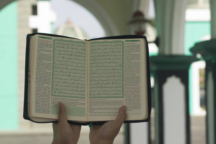 A woman holds aloft an opened copy of the Quran in a prayer space.