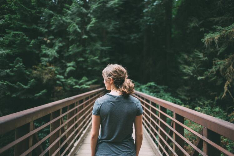 Woman walks along a bridge surrounded by trees