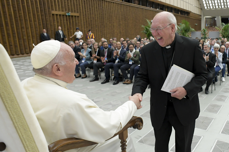 the pope and a cardinal shake hands and laugh in a vatican hall