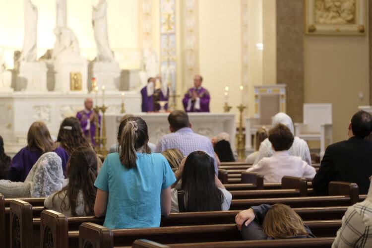 People sit in pews at Catholic Mass service as Bishop J. Mark Spalding in purple vestments consecrates the Eucharist in the background.