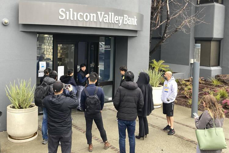 A representative of Silicon Valley Bank talks to people waiting outside the bank in Santa Clara, Calif., on March 10, 2023. The nation's 16th largest bank is the biggest to fail since the 2008 global financial meltdown. (AP Photo/Jeff Chiu, File)