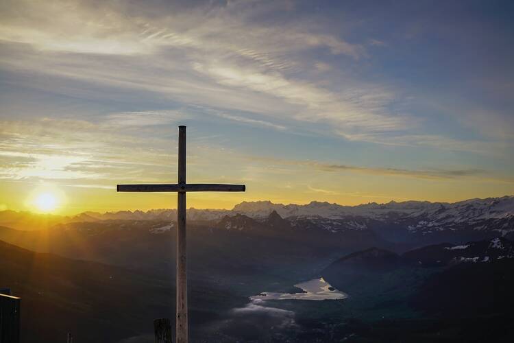 brown cross on a mountain with sun in the background