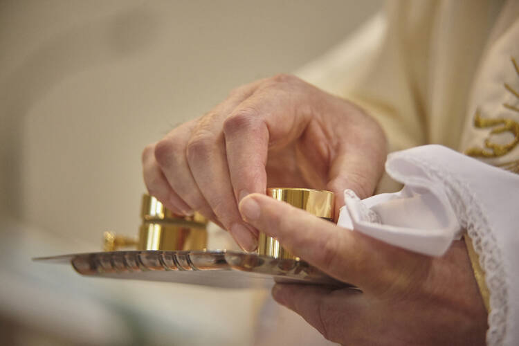 a priest's hand reaches into a gold container of chrism oil for confirmation