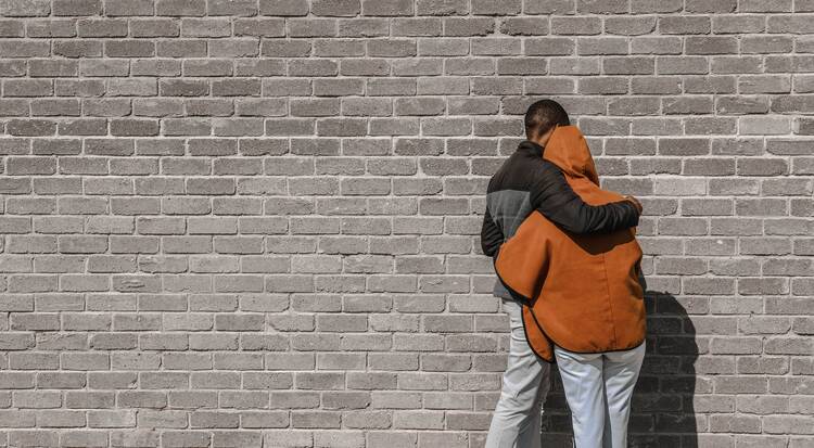 Two people hug reunited in front of a wall 
